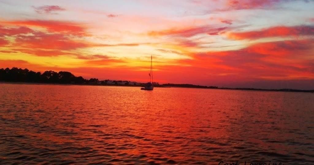 Sailboat silhouetted at vivid sunset over coastal bay waters