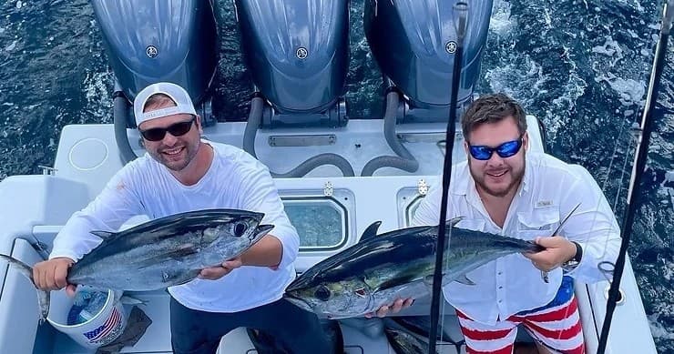 Two anglers holding tuna on sportfishing boat in open sea