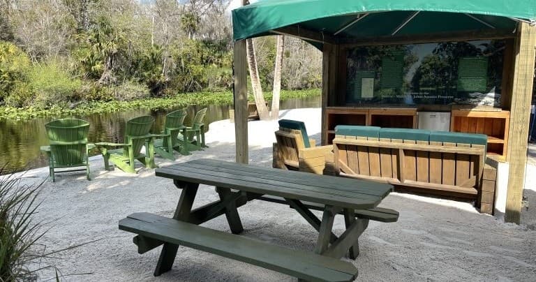 Picnic table under canopy beside calm river and seating