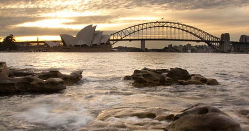 Sunset over Sydney Opera House and Harbour Bridge from rocky shore