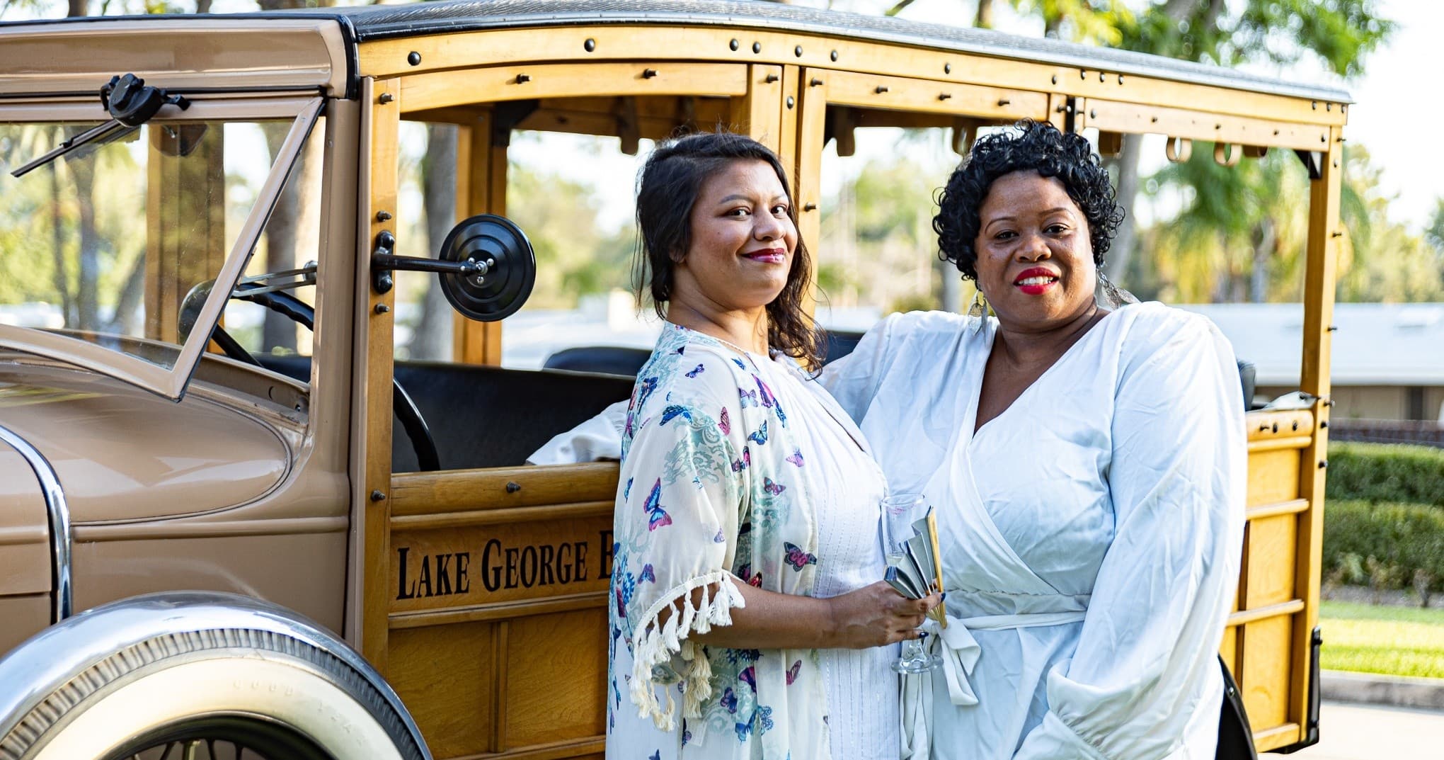 Two visitors posing by vintage woody car at historic estate garden