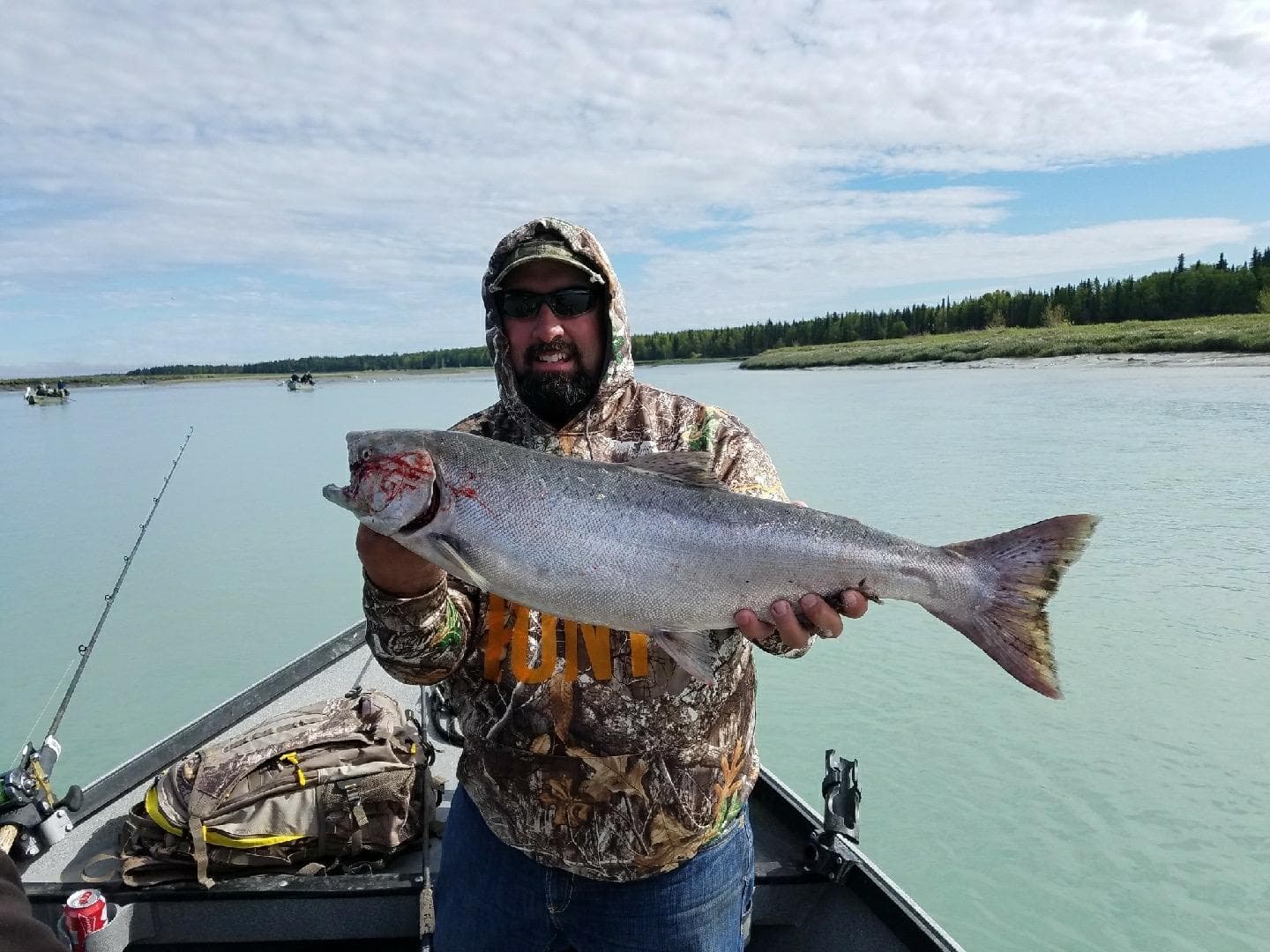 Angler holding salmon on boat in river under blue sky