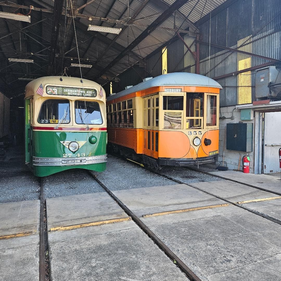 Green and orange streetcars stored in a shaded trolley barn interior
