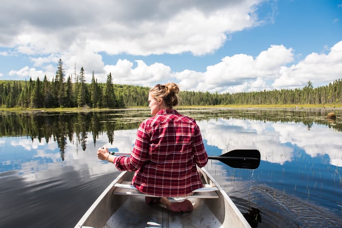 Solo canoeist paddling on mirror lake with forest shore