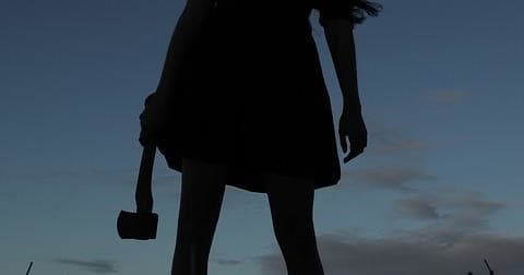 Silhouetted person holding sledgehammer at dusk in open field