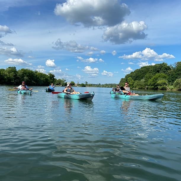 Kayakers paddling on calm green lake with tree-lined shore