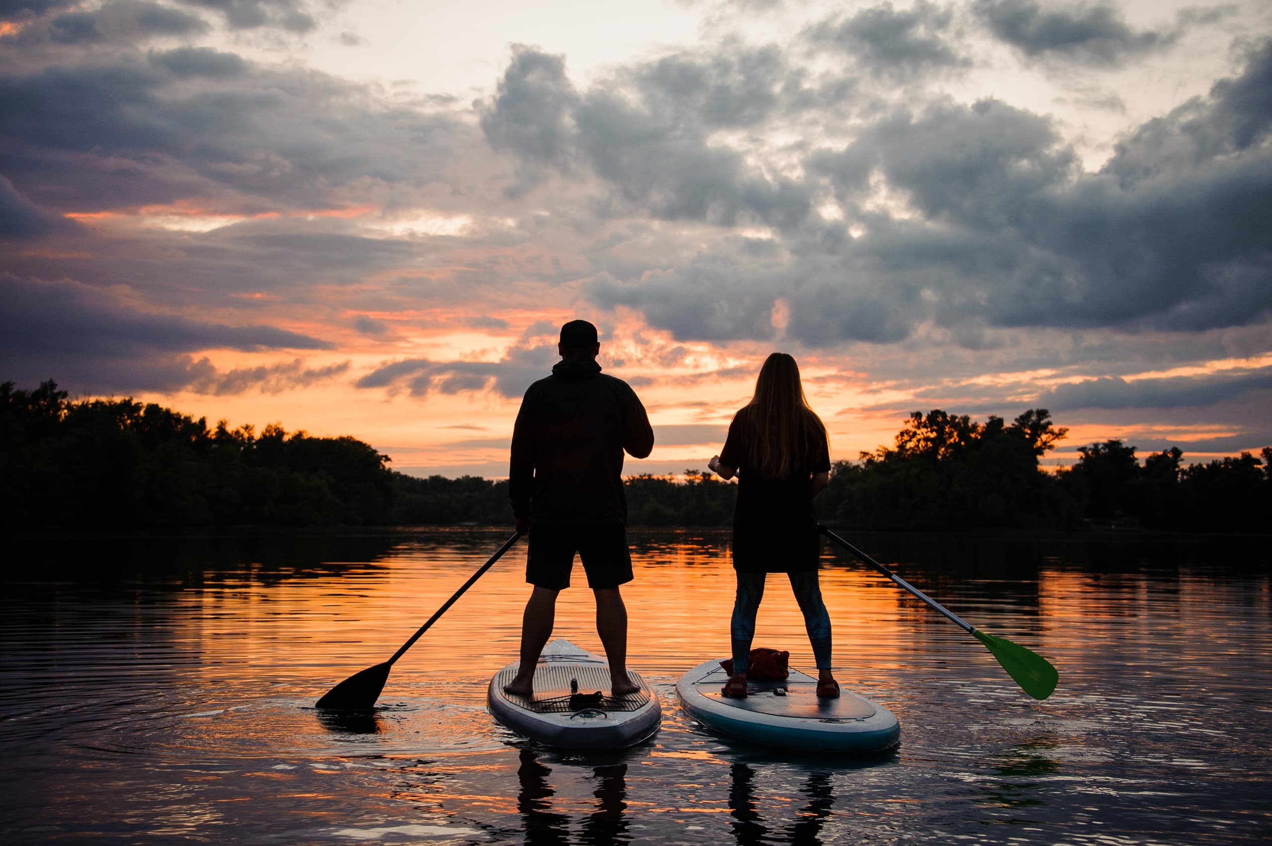 Couple stand-up paddleboarding at sunset on tranquil lake