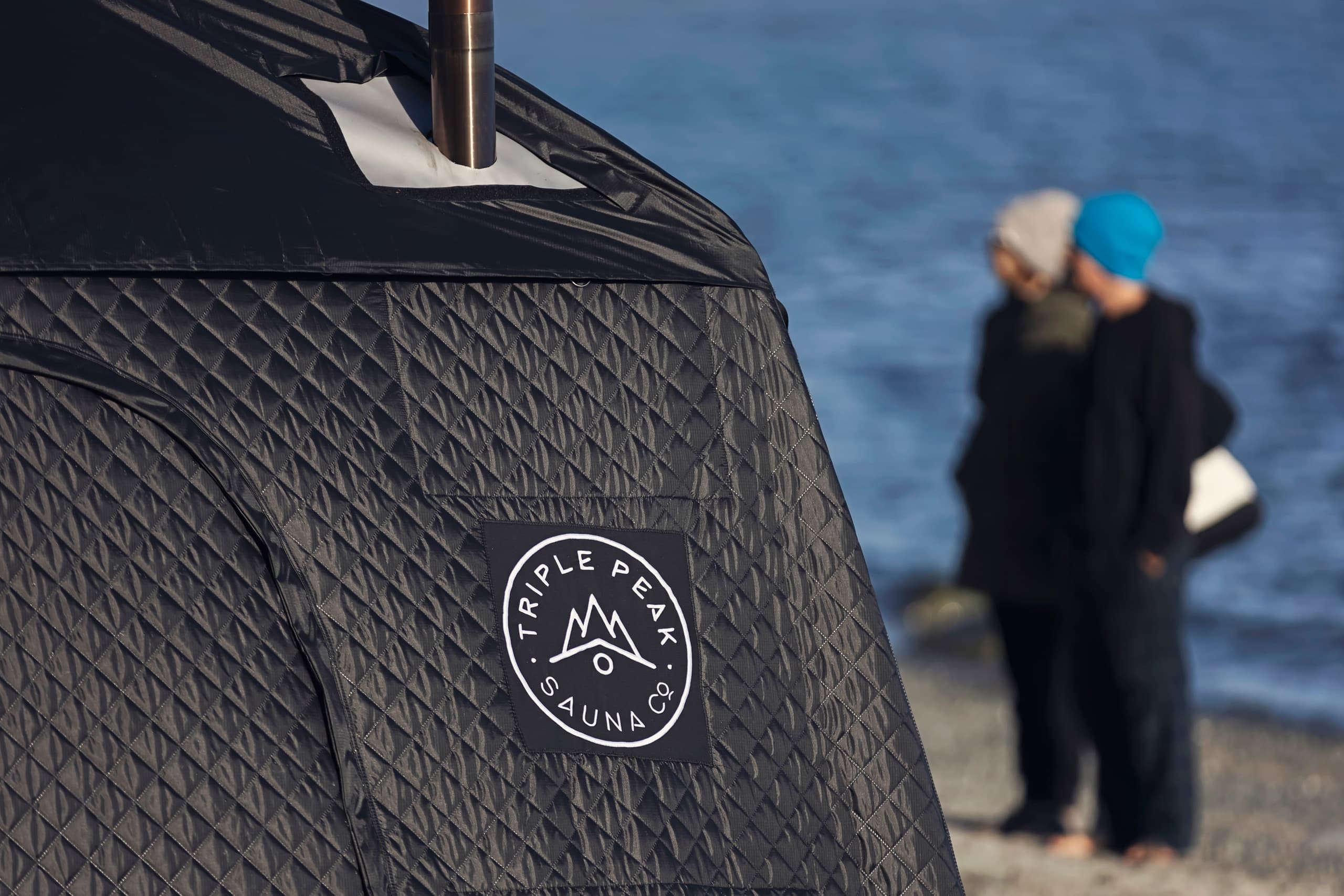 Textured portable sauna tent with logo on coastal beach backdrop