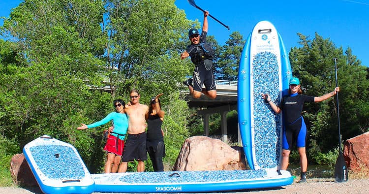 Group paddlers posing on shore with large inflatable SUP by trees