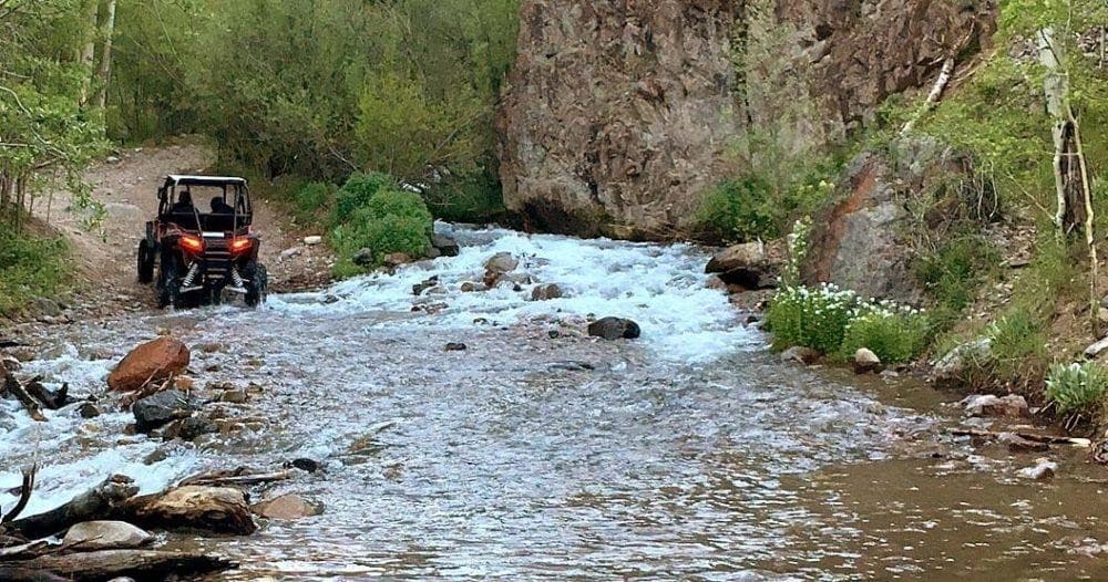 UTV crossing shallow mountain creek river in aspen forest