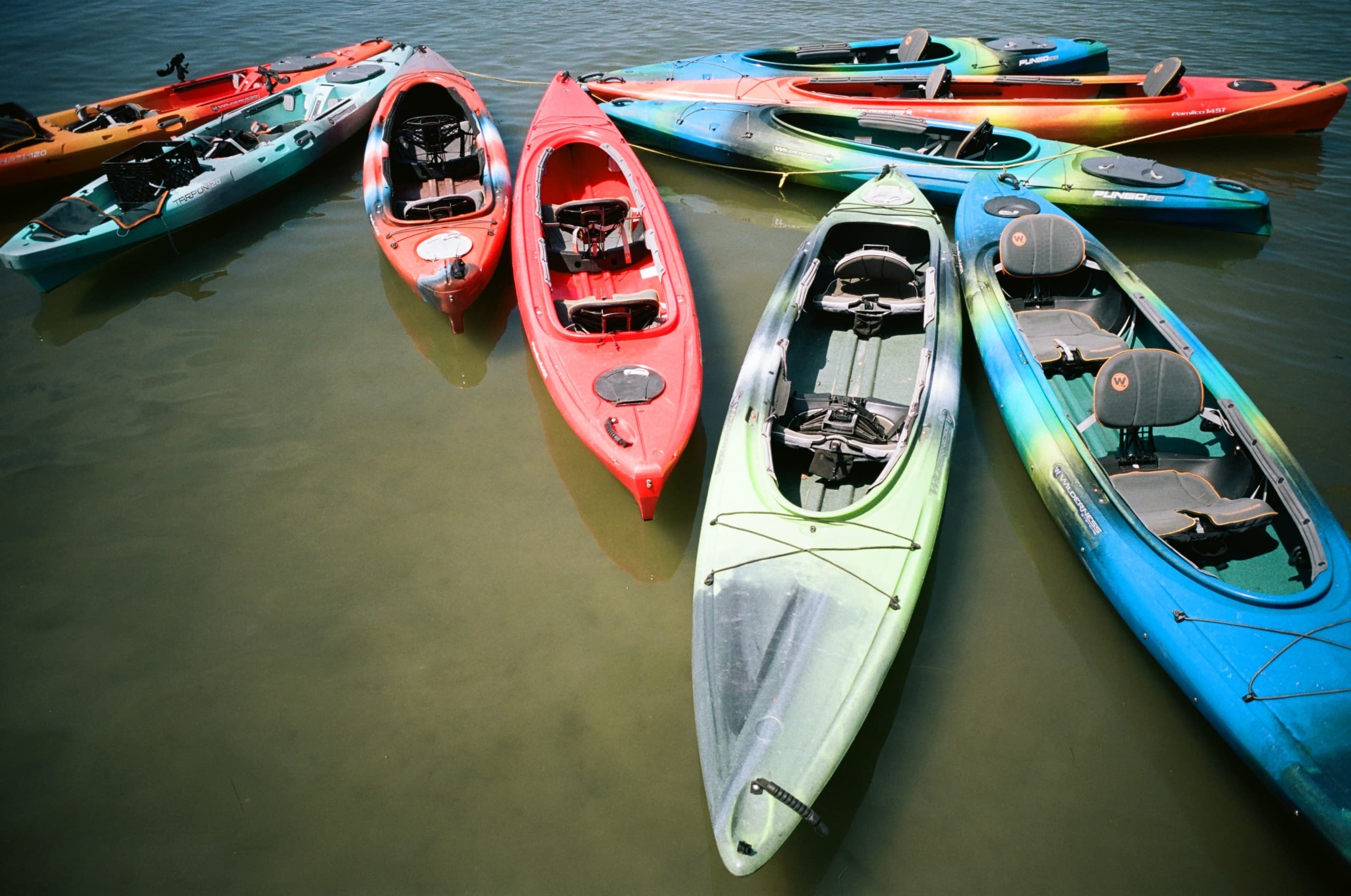 Colorful kayaks clustered on shallow beach water, aerial view