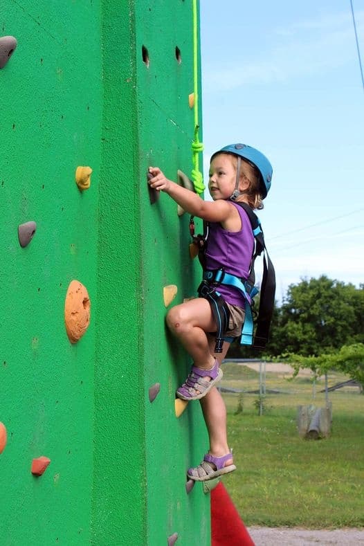 Child rock climbing on outdoor artificial wall with safety gear