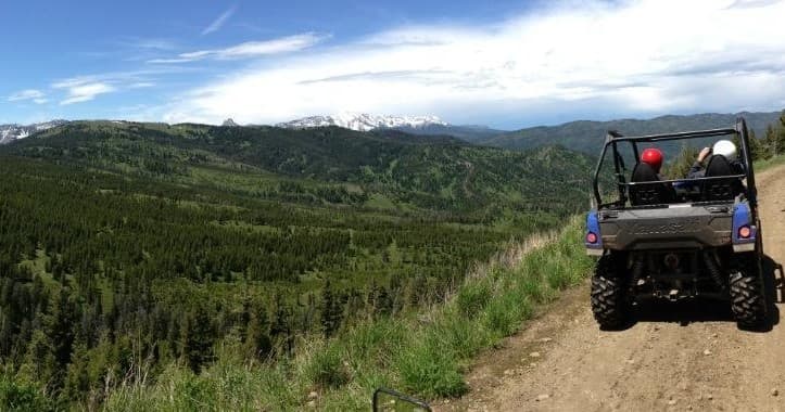 UTV riding on mountain trail over verdant forested valley