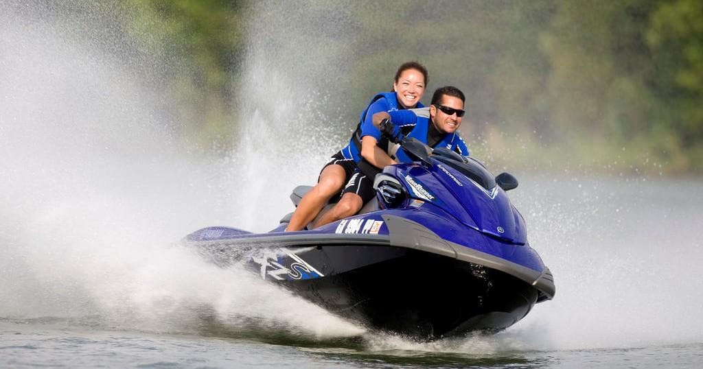 Couple riding a blue jet ski with water spray on lake or river