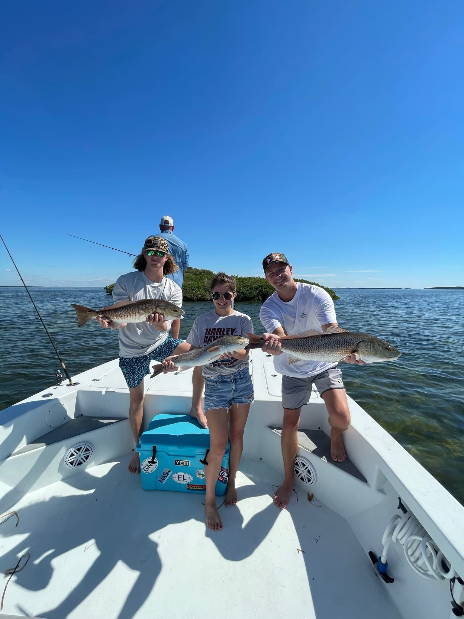 Family fishing for redfish on shallow coastal flats under blue sky