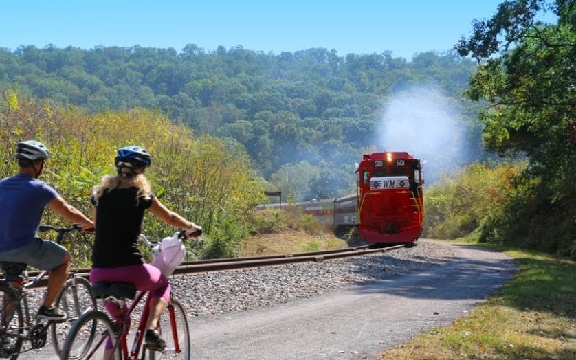 Cyclists watching vintage red train pass through scenic valley