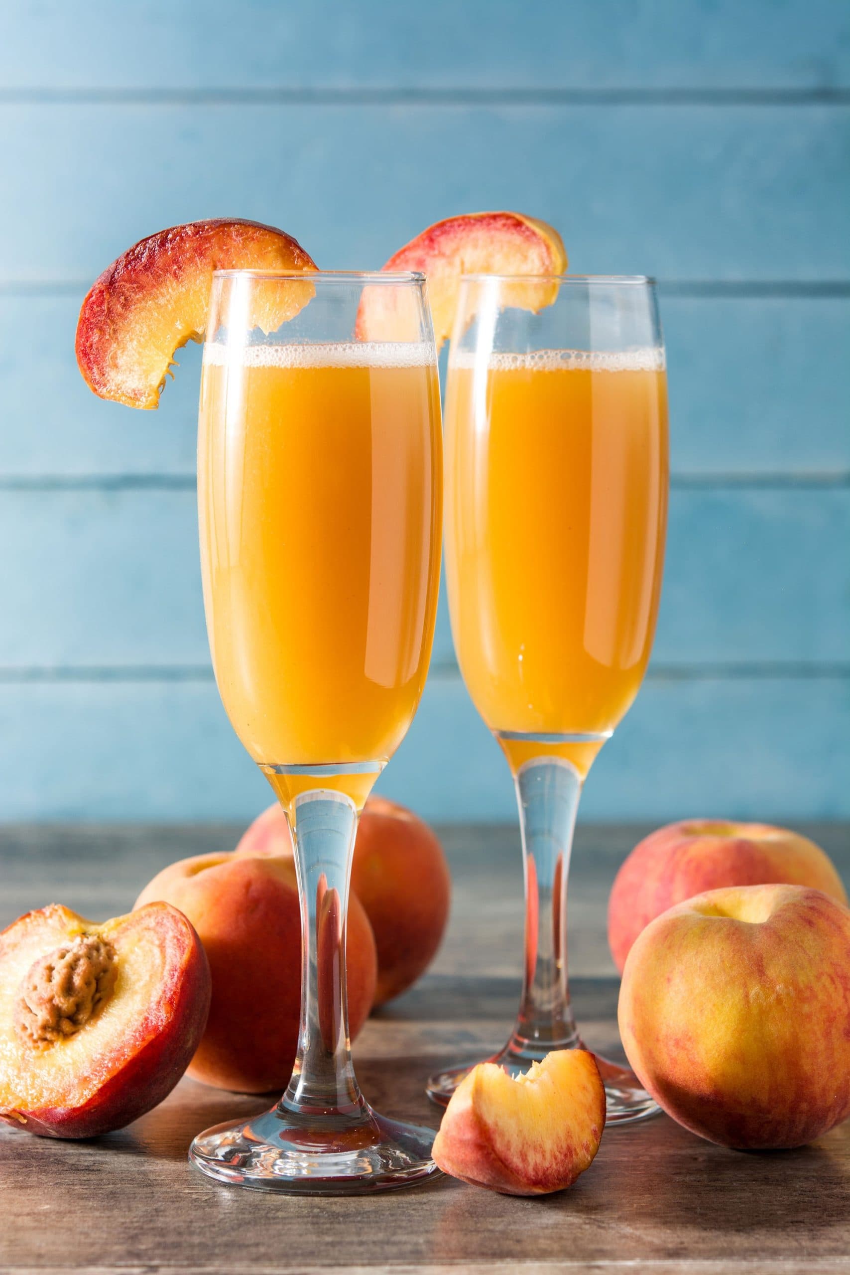 Peach mimosas in champagne flutes with fresh peaches on table