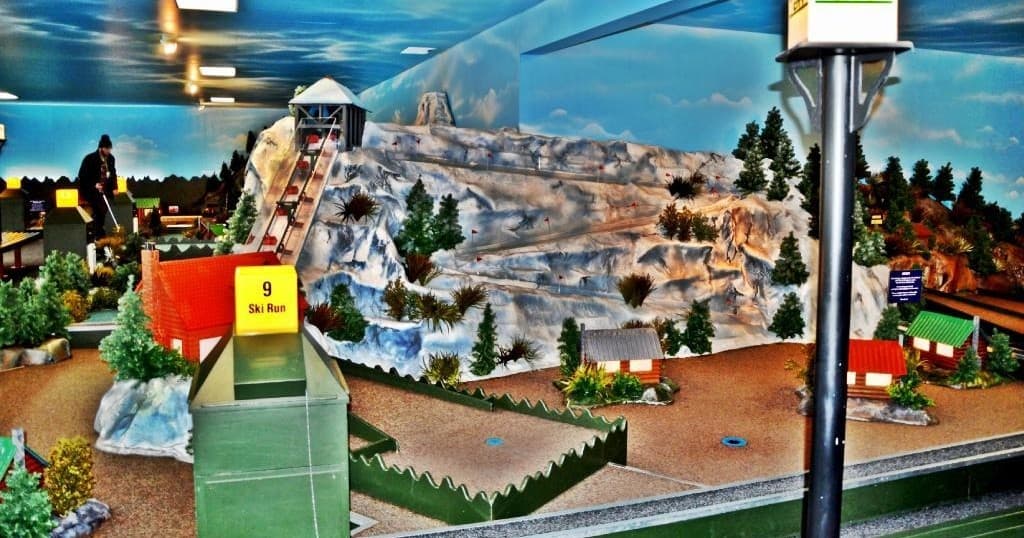 Themed mini golf hole with mountain mural backdrop, indoor play