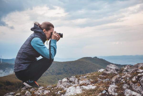 Photographer shooting mountain vista on rocky ridge at sunset