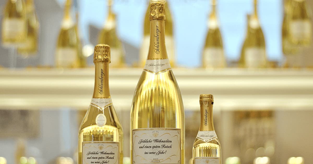 Rows of sparkling wine bottles displayed on reflective shelf indoors