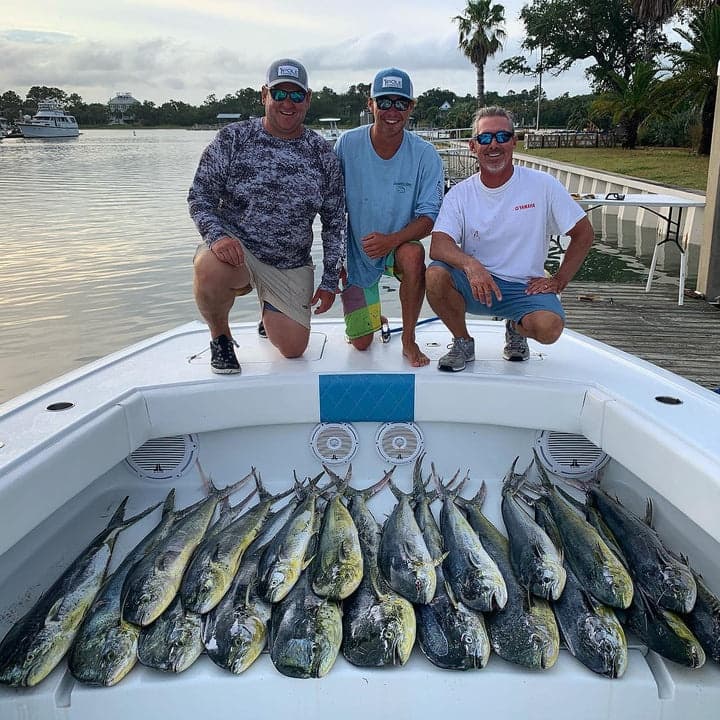 Three anglers posing with dozens of mahi mahi on boat floor