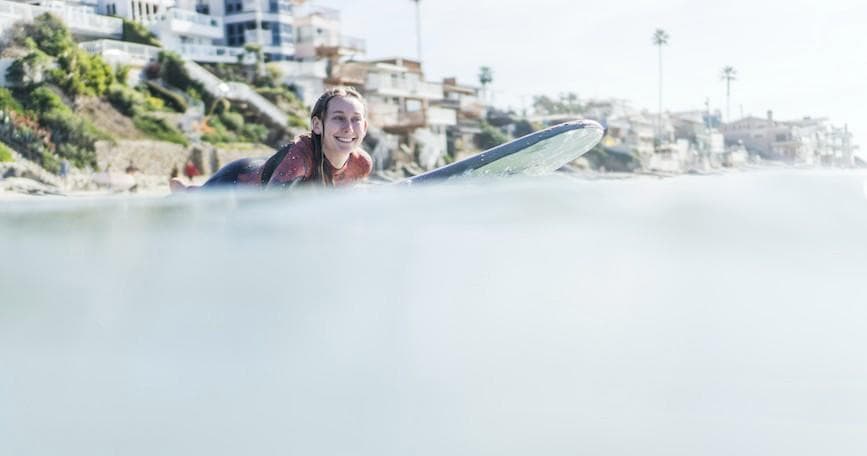 Surfer paddling on surfboard in calm coastal water, beach town