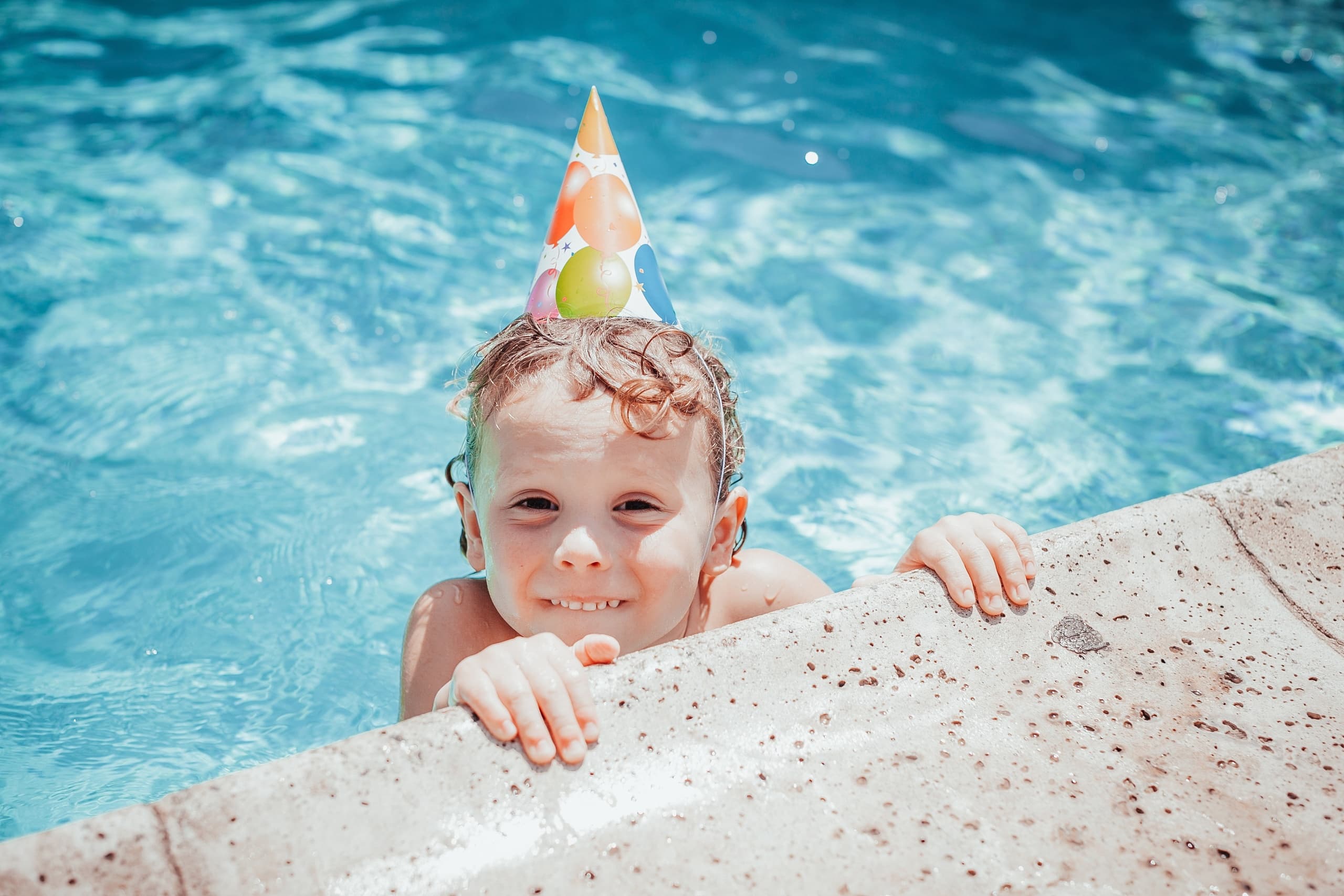 Child in pool wearing party hat at poolside celebration