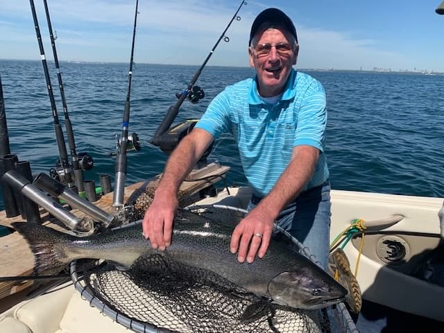 Angler holding large salmon on boat with open lake background