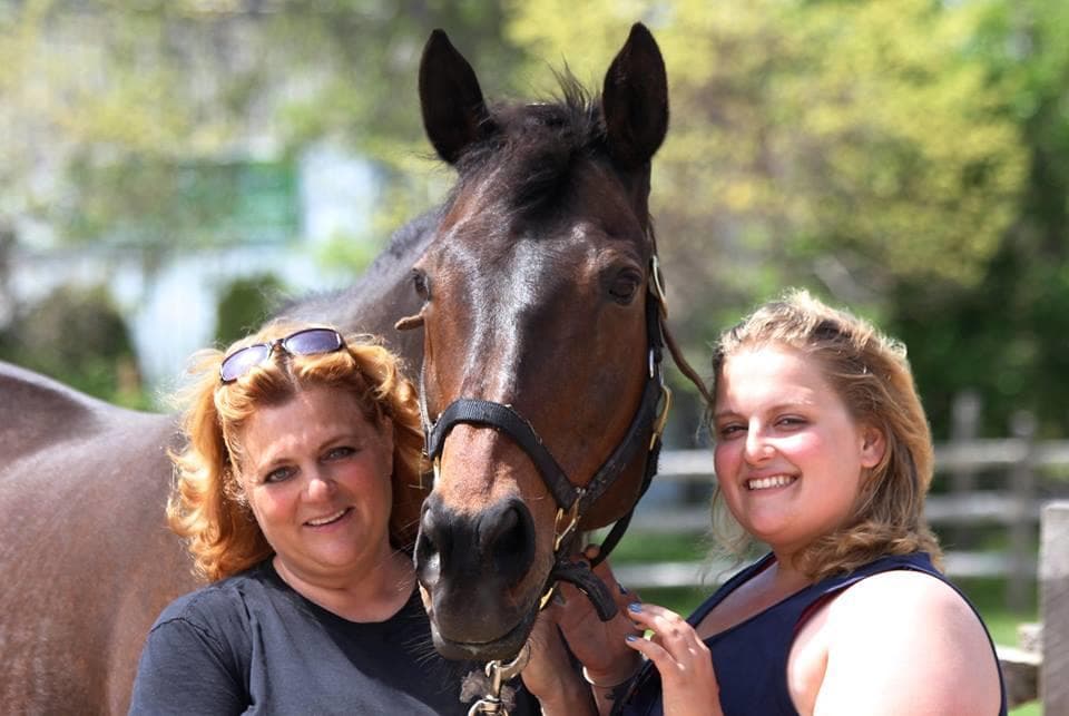 Women with rescued horse smiling together at outdoor ranch paddock