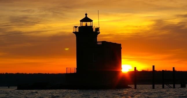Sunset lighthouse silhouette on coastal pier at sea, scenic view