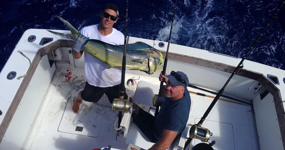 Anglers holding mahi mahi on sportfishing boat off Kauai coast
