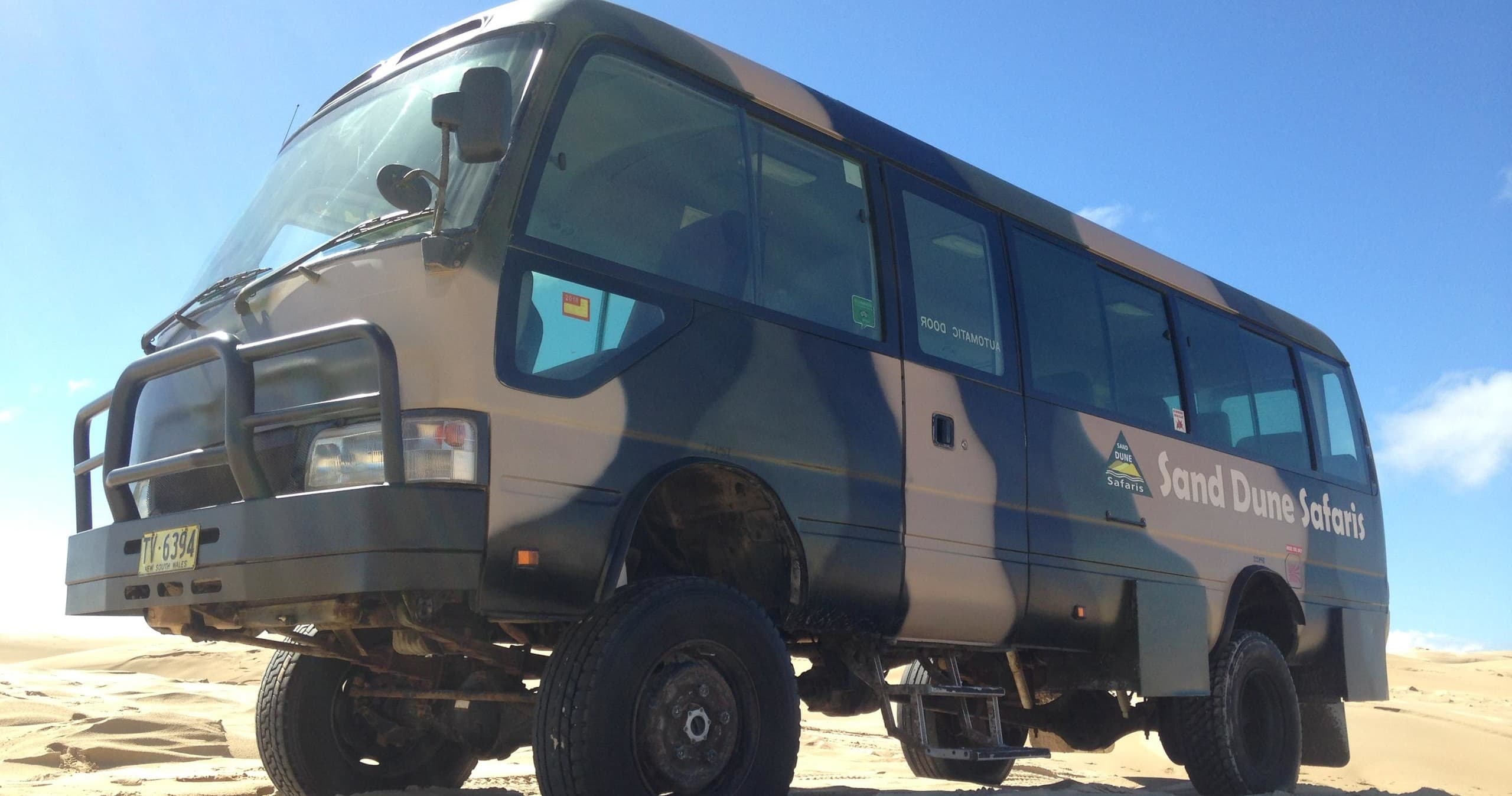 4x4 safari bus traversing sandy dunes under clear blue sky