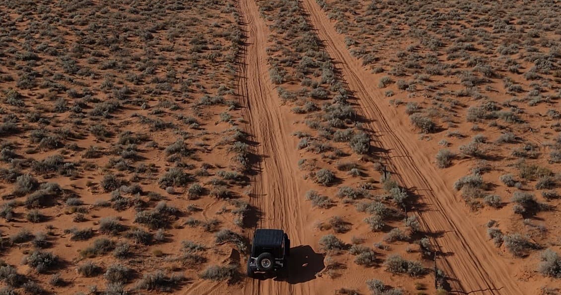 Overhead desert tracks with lone 4x4 vehicle exploring red plains