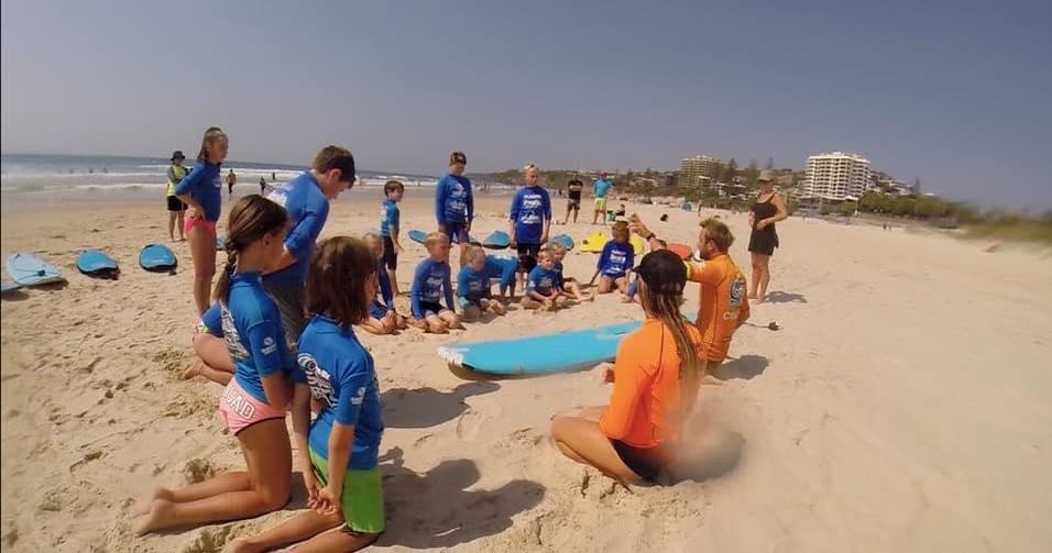 Group surf lesson on beach with instructors teaching kids coastal skills