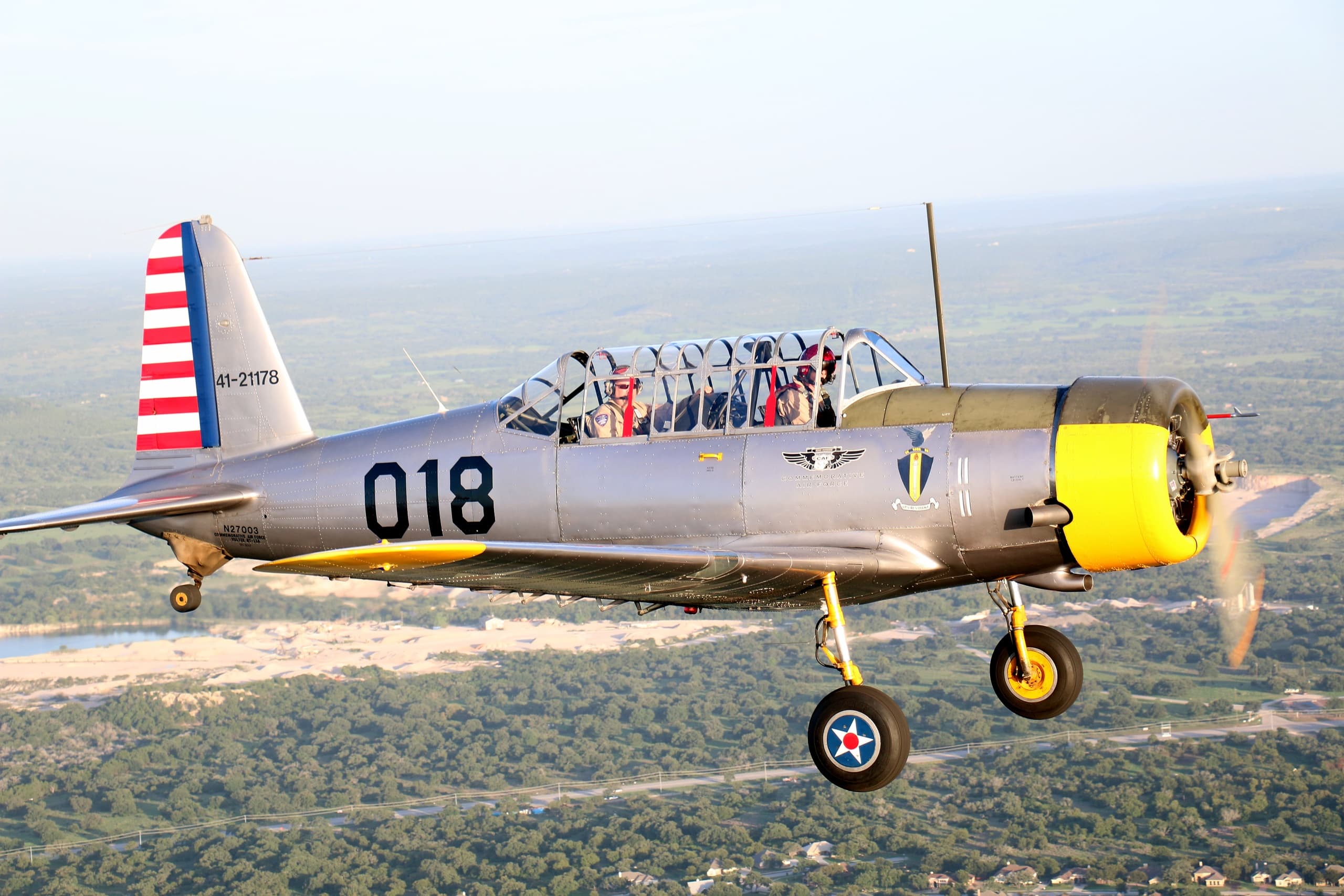 Historic silver trainer plane (018) cruising over patchwork fields and trees