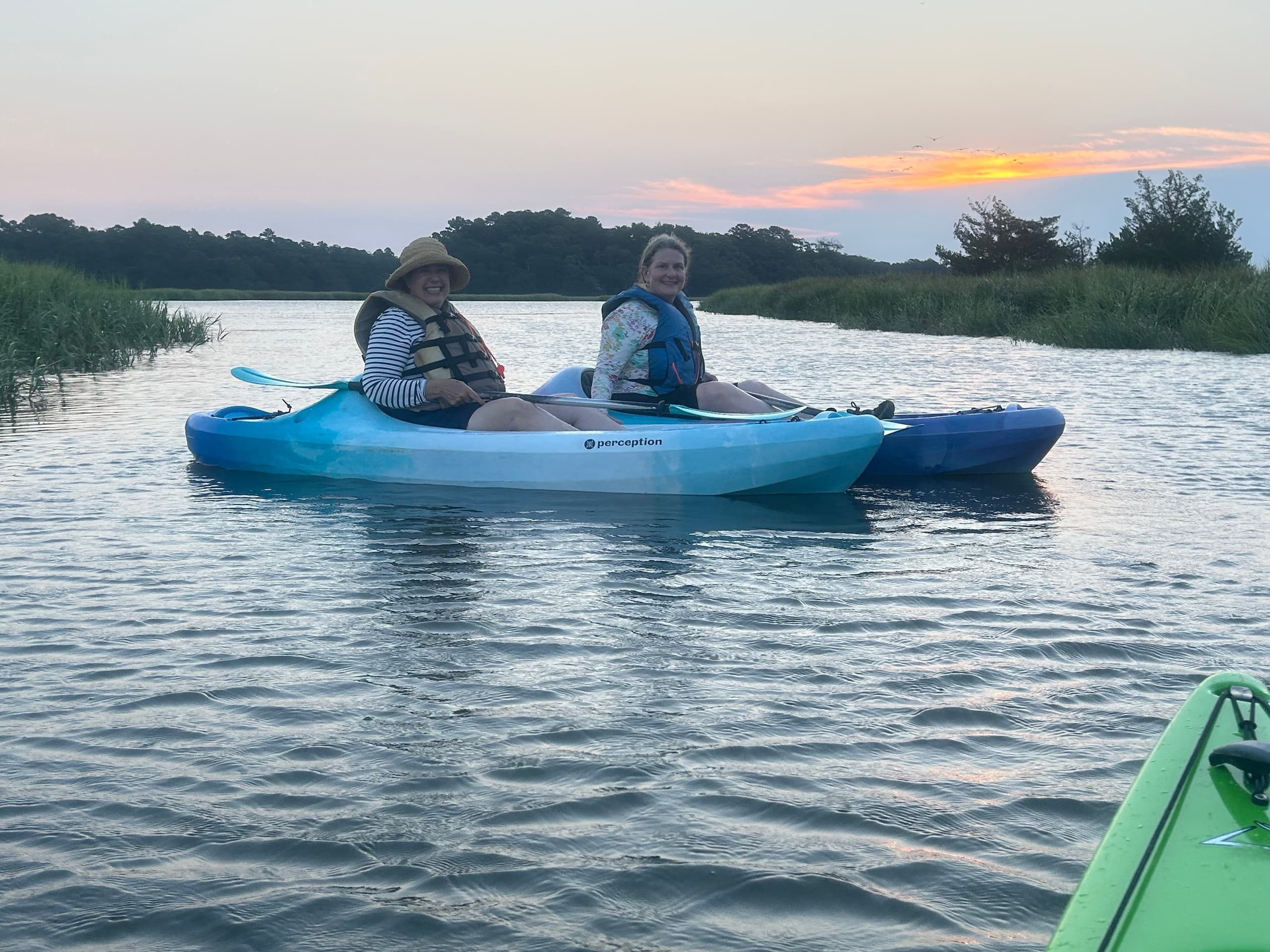 Two kayakers paddling at sunset in serene marshy inlet