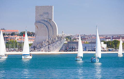 Fleet of sailboats sailing past Lisbon's riverside monument