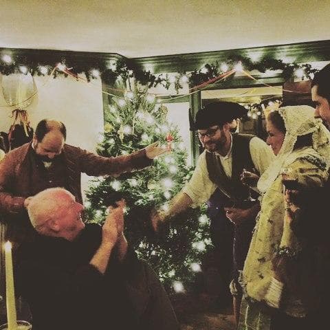 Victorian holiday reenactors gathered by decorated indoor tree