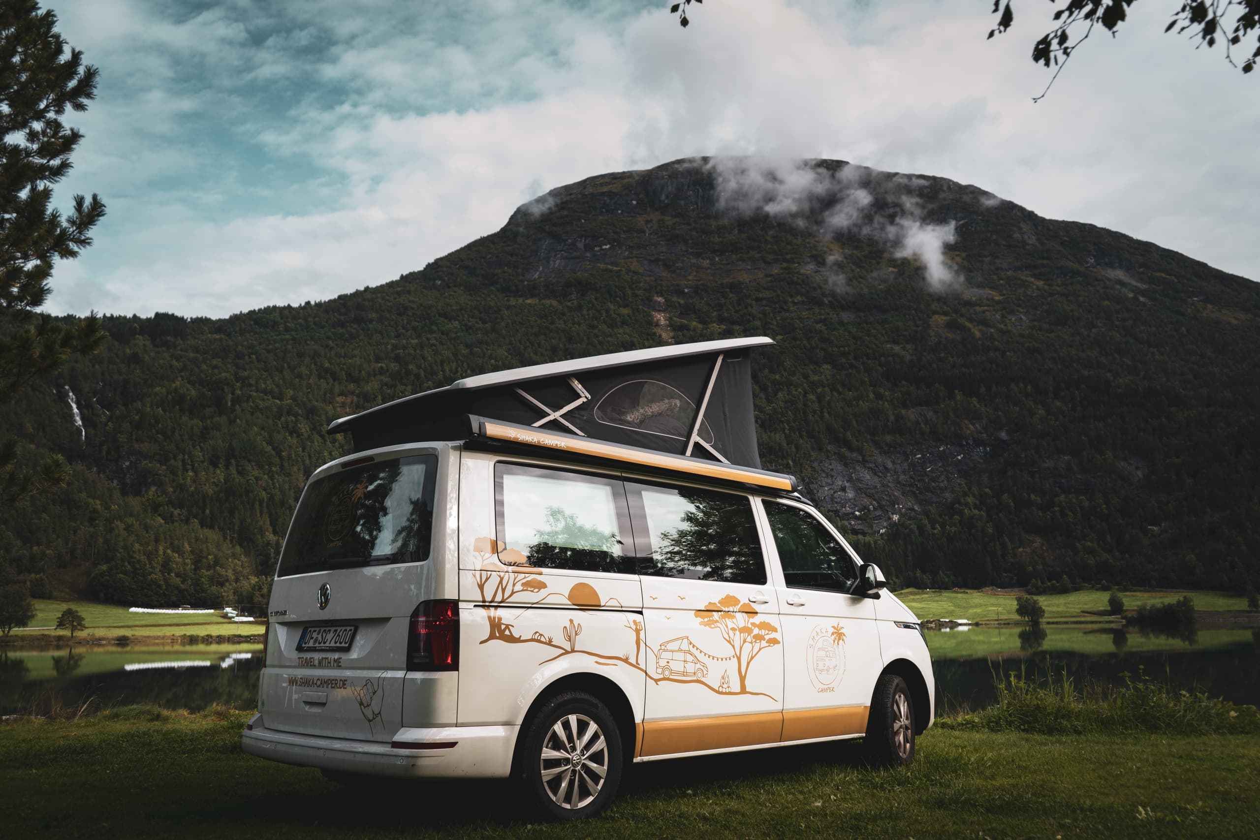 Camper van with pop-up roof parked by alpine lake and mountains