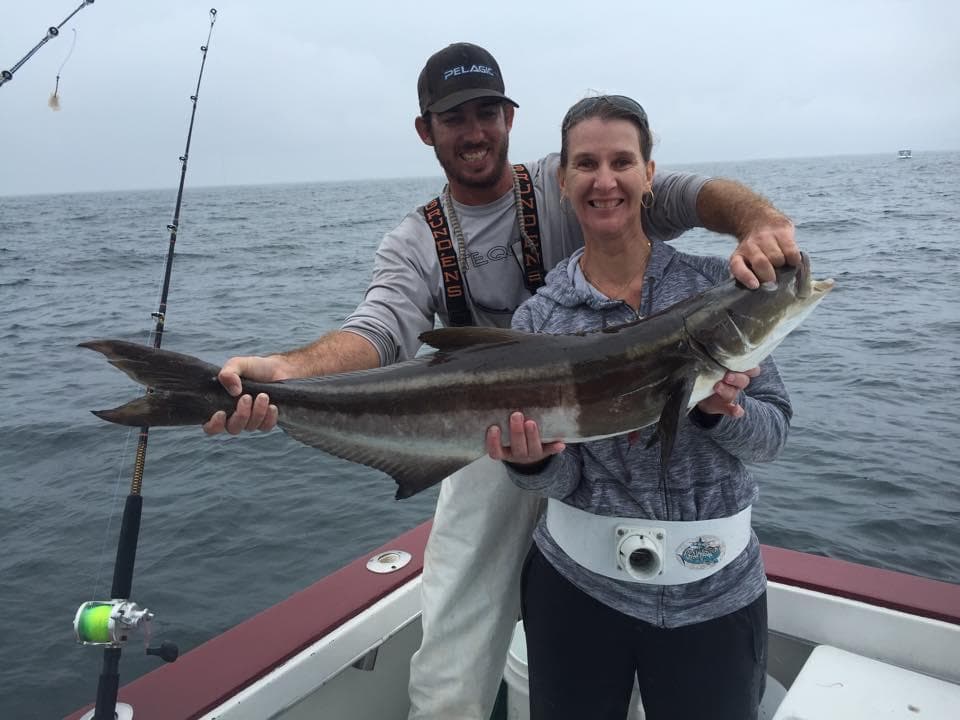 Two anglers holding a large offshore fish on a charter boat