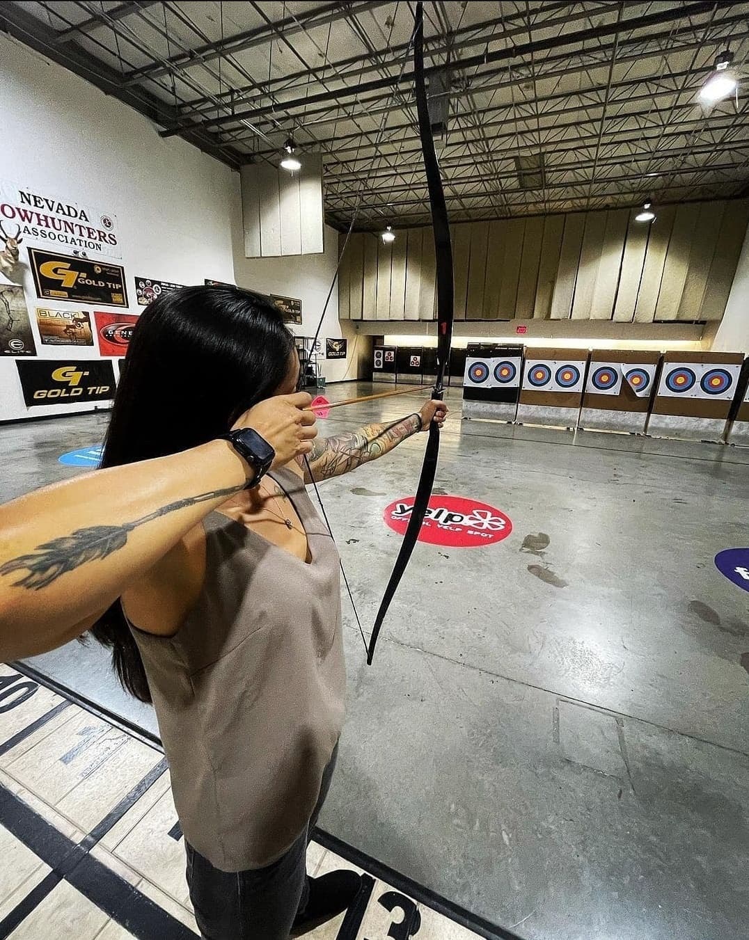 Close-up archer drawing recurve bow inside indoor target range