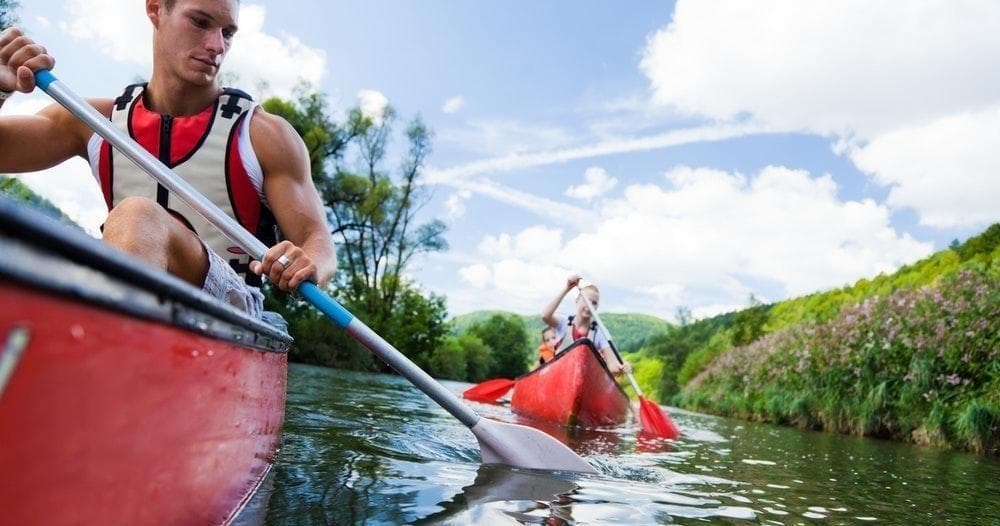 Two kayakers paddling through green river channel on trip