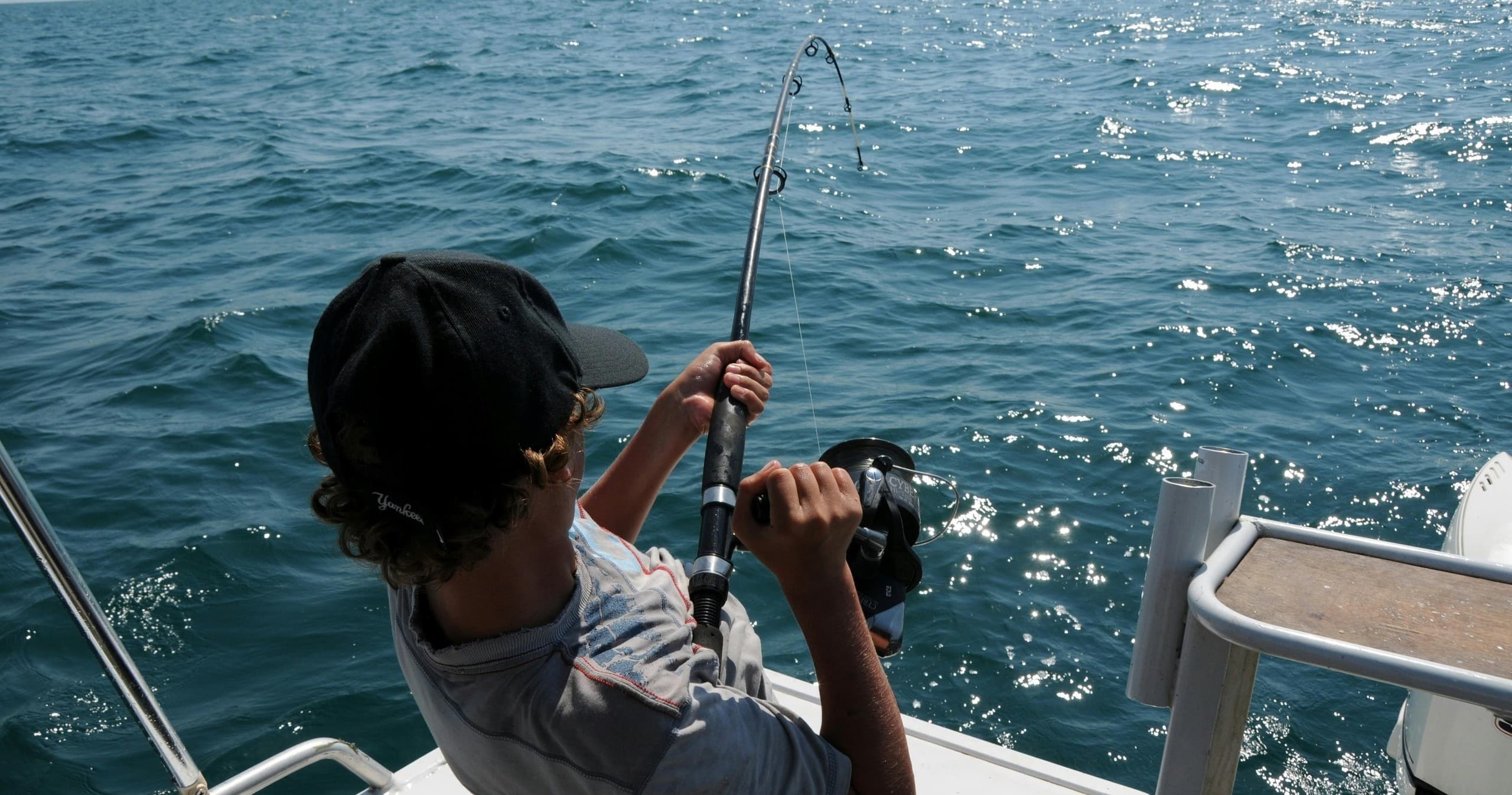 Child reeling in fish aboard a family fishing boat on open sea