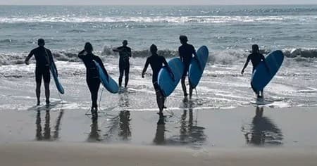 Surf trainees carrying boards into surf at sandy beach shoreline