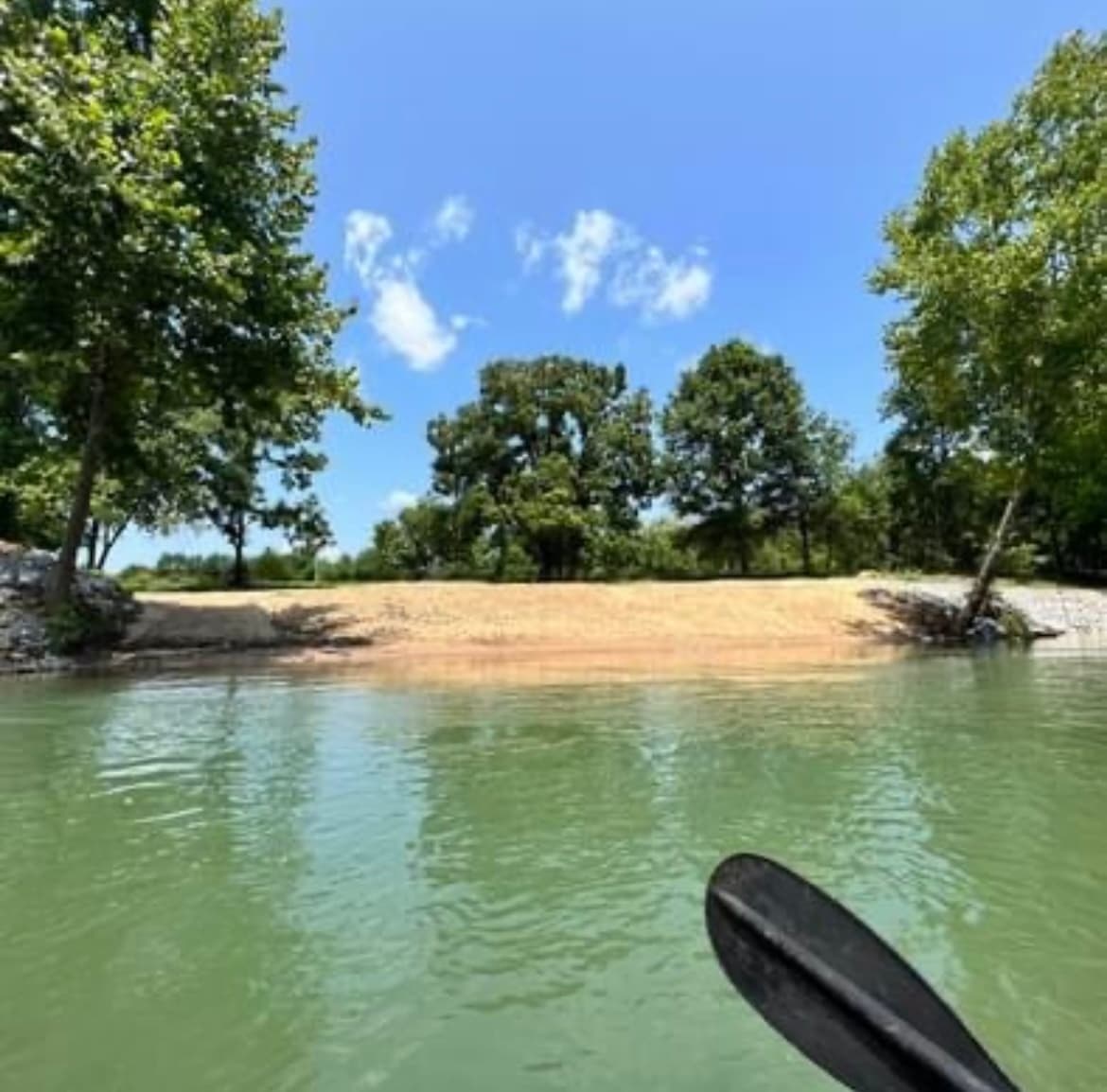 Kayak approaching sandy river sandbar under leafy trees