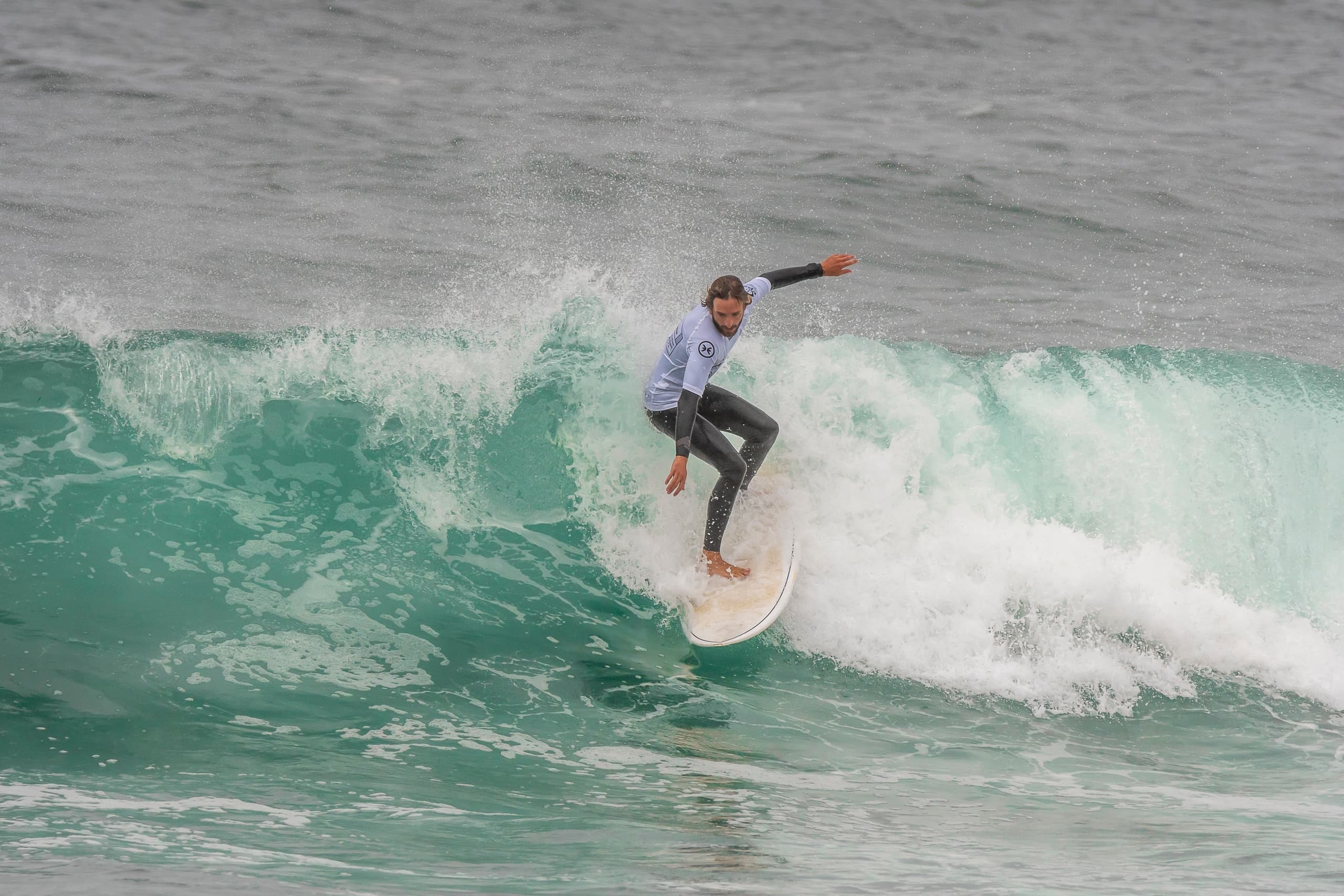 Surfer carving a turquoise ocean wave off a sandy coast