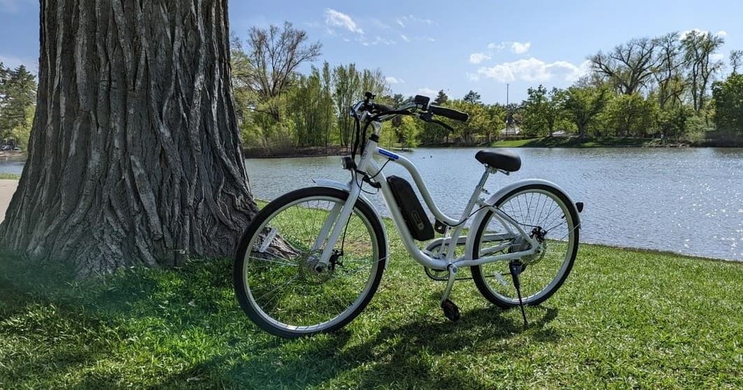 White electric bike leaning by large tree on lakeside greenway