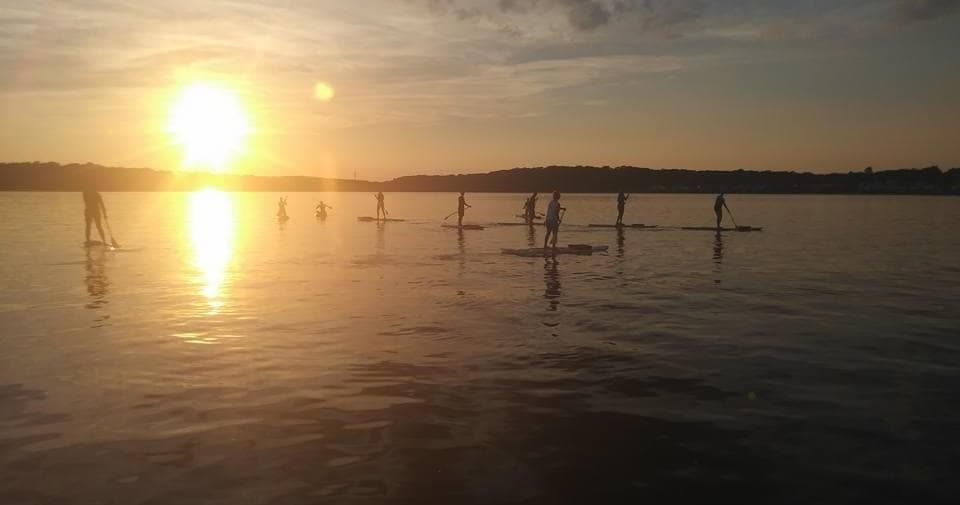 Sunset over bay with distant paddleboarders silhouetted