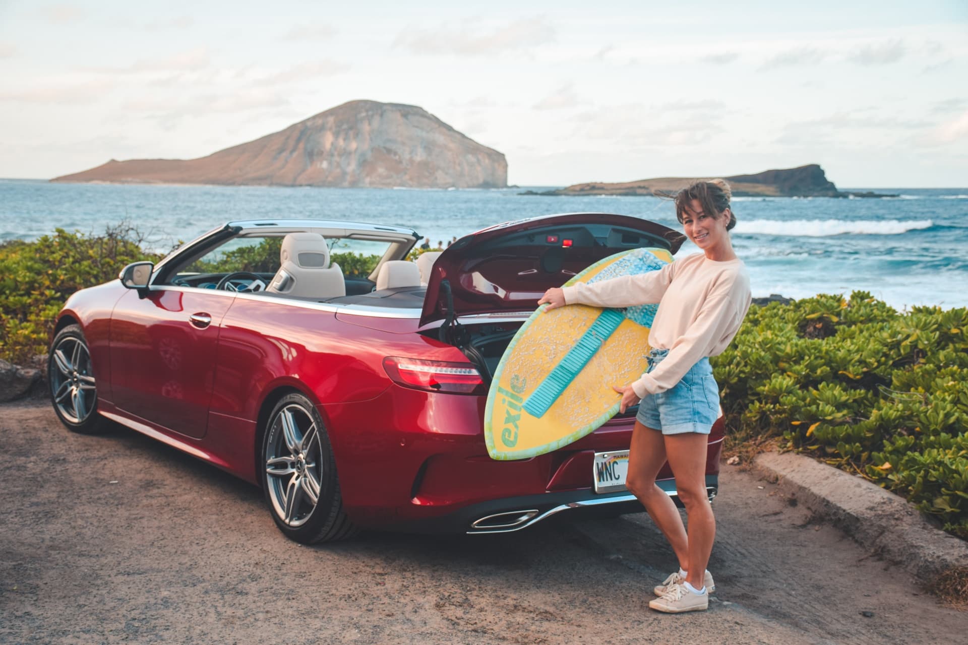 Surfer loading board into red convertible at Oahu beach parking