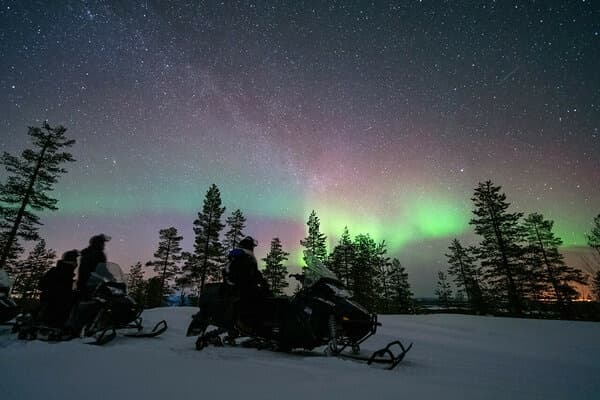Snowmobile silhouettes under Northern Lights in Lapland